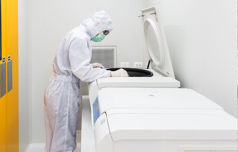 Lab worker in suit looking into large equipment