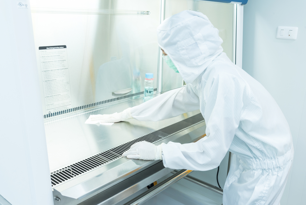 worker in coverall gown cleaning a biosafety cabinet for decontamination services