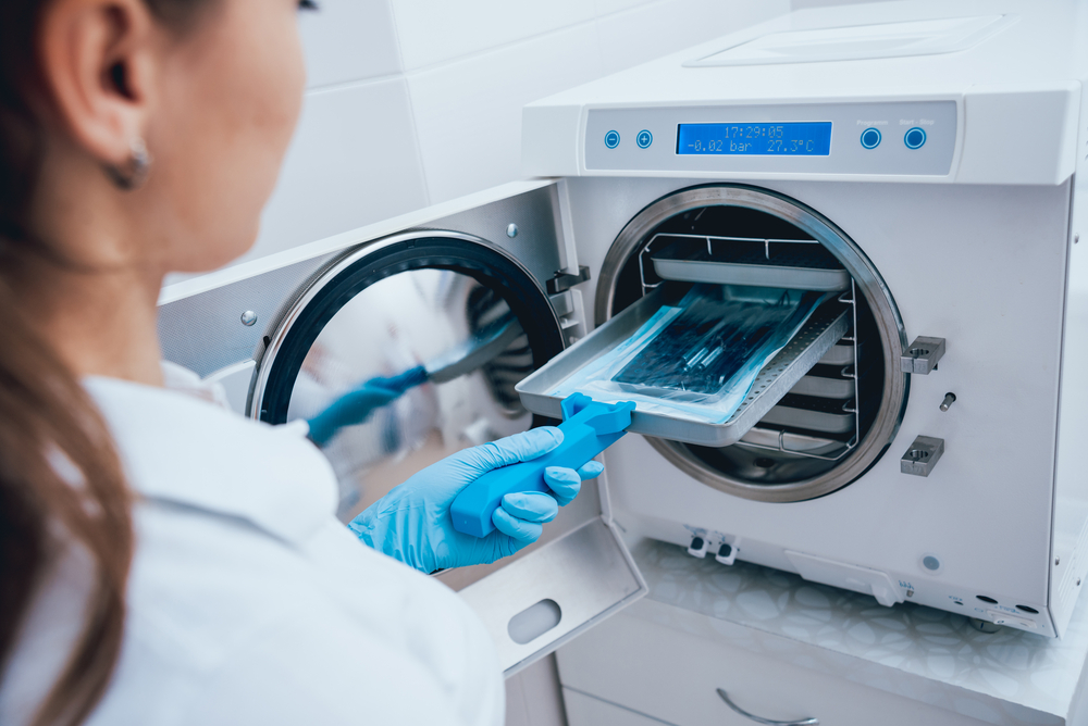 Female lab worker sterilizing medical instruments in autoclave