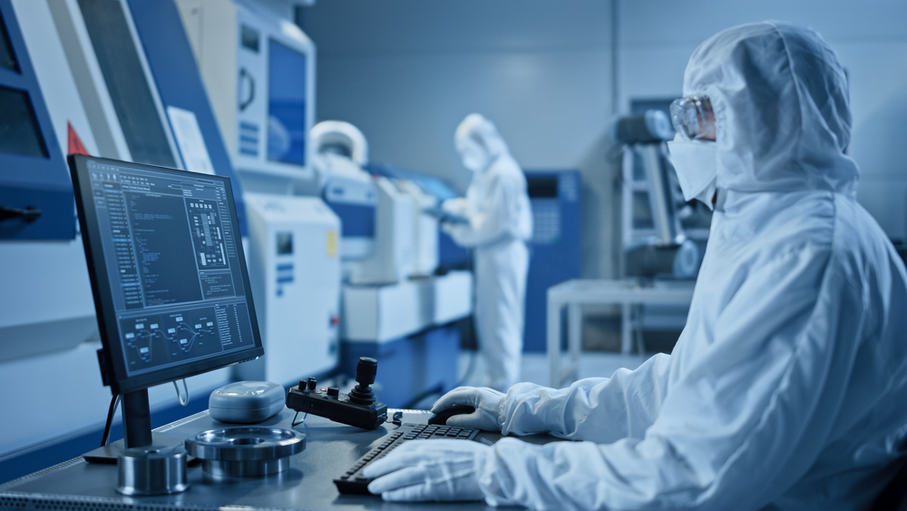 Factory Cleanroom: Engineer Wearing Coverall and Mask Does System Control on a Computer, Uses Controller, Screen Shows Infographics