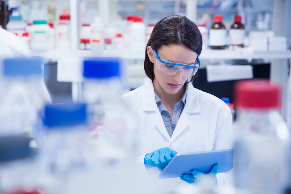 Chemist wearing safety glasses and using tablet pc in lab, Testing for Coronavirus Covid19 vaccine