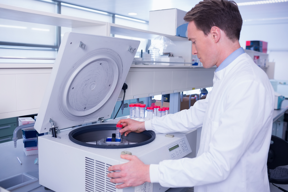 Chemist in lab coat using a centrifuge in laboratory